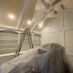 Interior painting in progress with protective coverings and a ladder